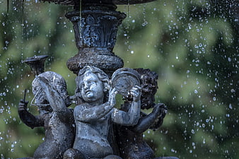 Close-up of weathered cherub statues on a garden fountain with water droplets