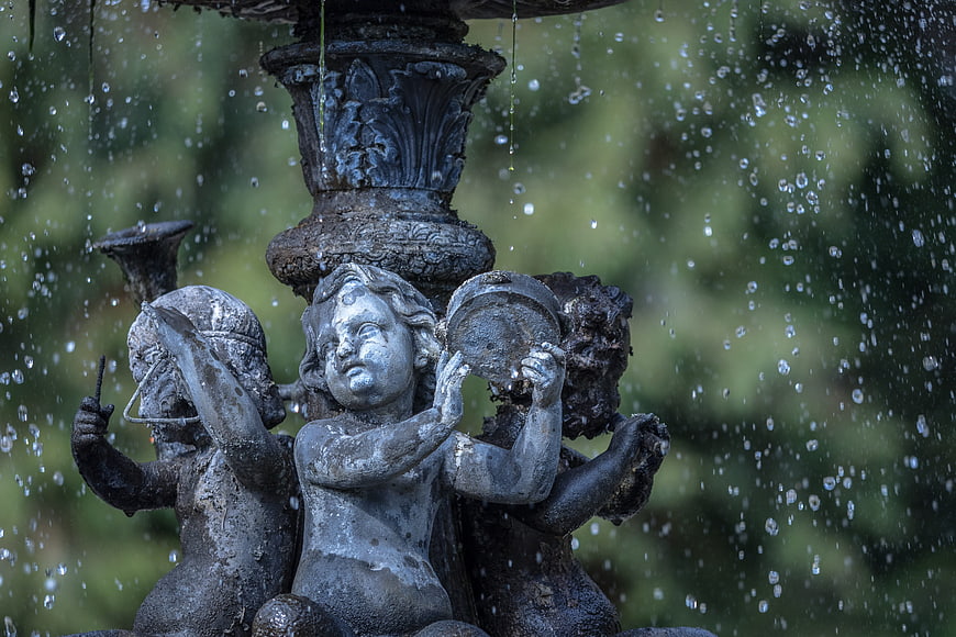 Close-up of weathered cherub statues on a garden fountain with water droplets