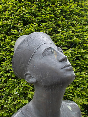 Bronze Sculpture of Woman's Head Against Green Leaves