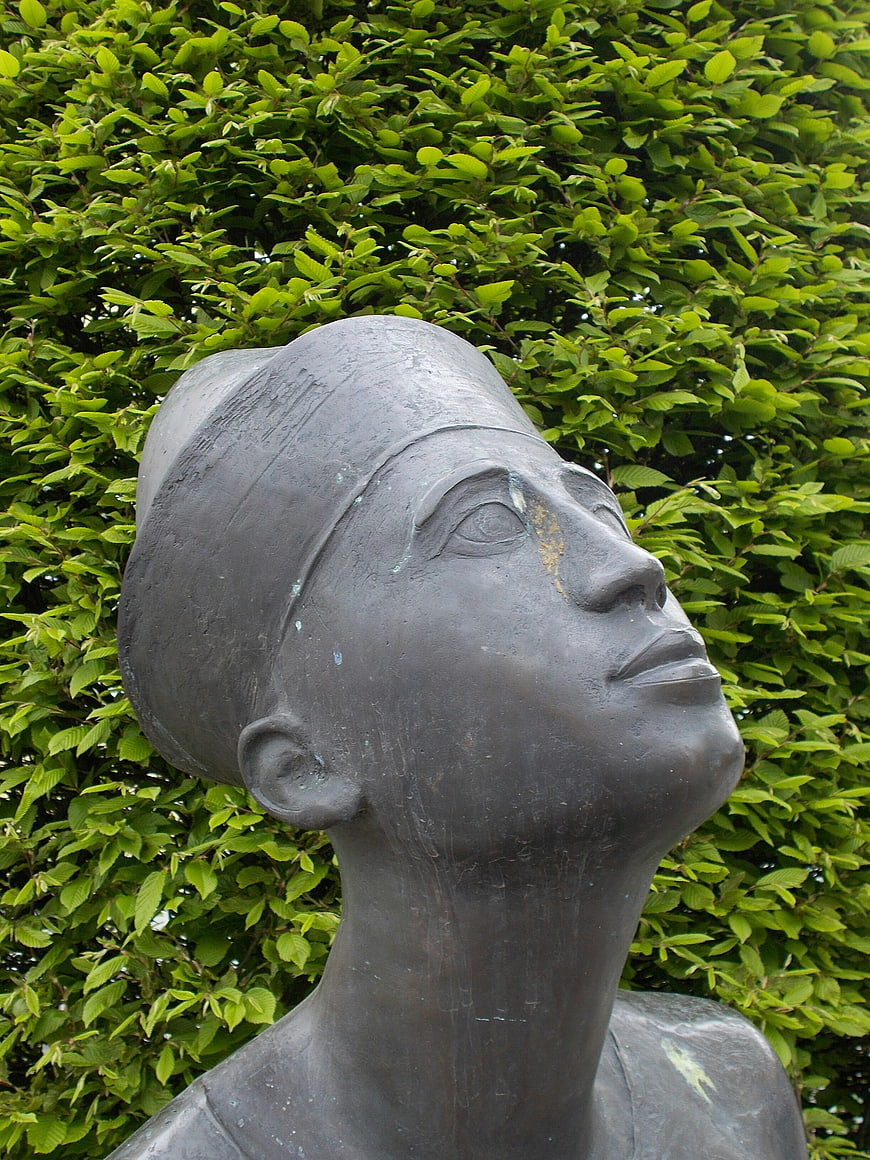 Bronze Sculpture of Woman's Head Against Green Leaves