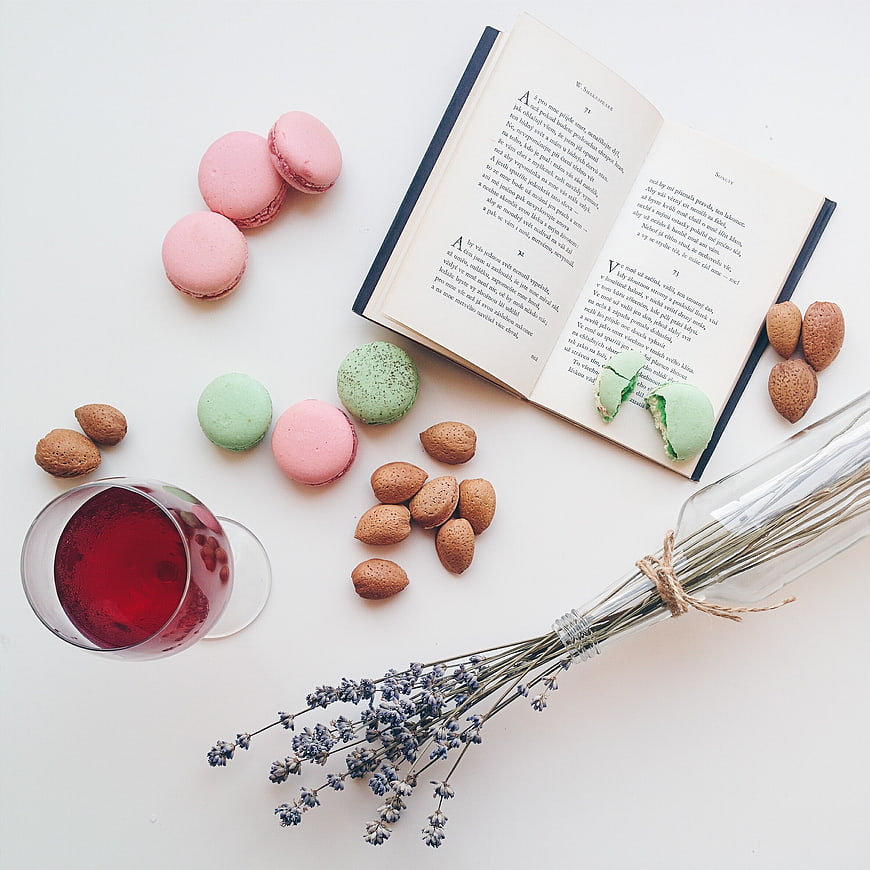 Flat lay of macarons, book, wine, and lavender on white background