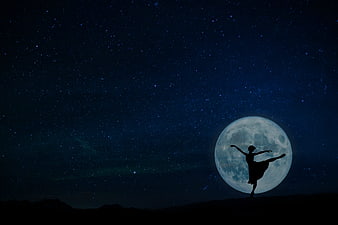 Silhouette of a ballerina dancing in front of a full moon and starry night sky