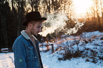 Young Man Smoking in Snowy Forest at Sunset