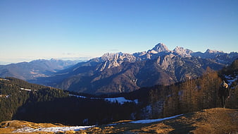 Hiker on Mountain Ridge with Snowy Peaks and Forest Valley