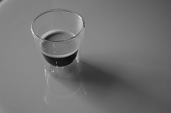 Black and white shot glass with espresso on reflective surface