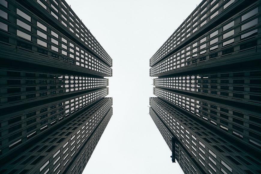 Symmetrical low angle view of modern skyscrapers against white sky
