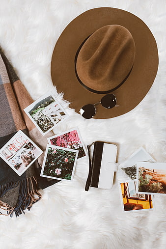 Flat lay of travel accessories, hat, and photos on white fur