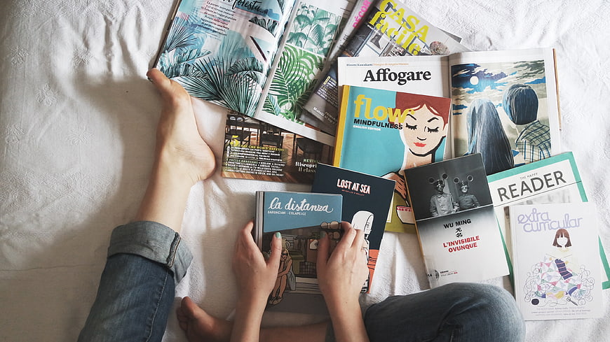Person reading books and magazines on a white bed