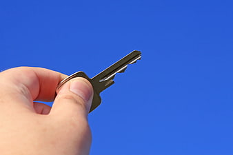 Hand Holding Silver Key Against Blue Sky Background