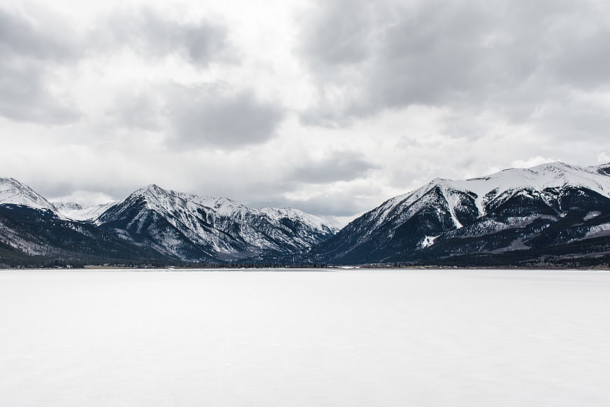 Snowy Mountain Landscape with Frozen Lake and Cloudy Sky
