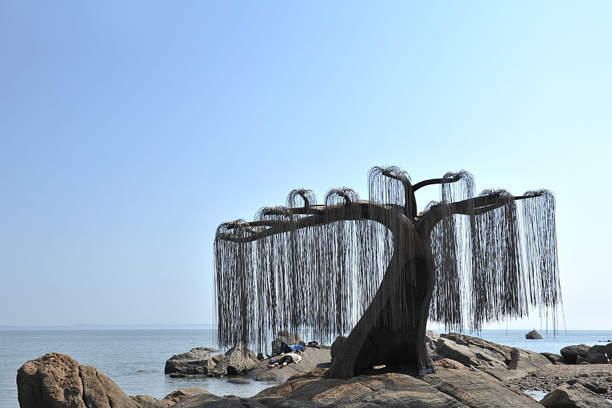 Metal willow tree sculpture on rocky ocean shore