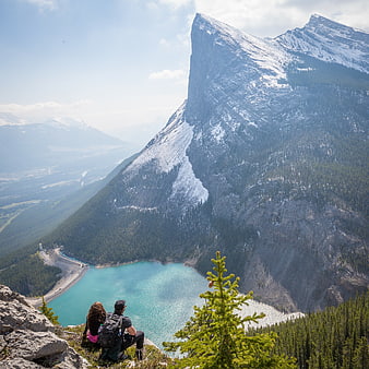 Couple hiking overlooking turquoise mountain lake and snowy peaks