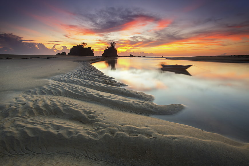 Serene Sunset Beach with Silhouetted Boat and Rocky Islands