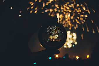 Hand holding crystal ball with fireworks reflection at night