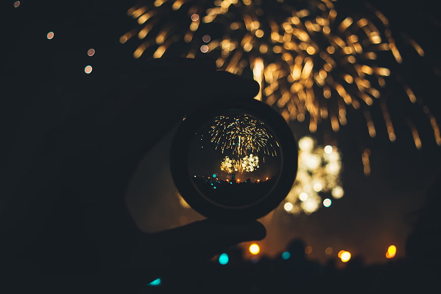 Hand holding crystal ball with fireworks reflection at night