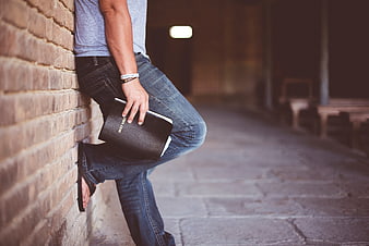 Man leaning against brick wall holding black bible
