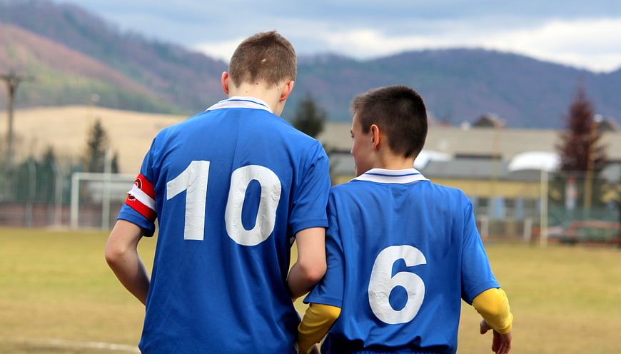Two Young Boys in Blue Football Jerseys Walking on Grass Field