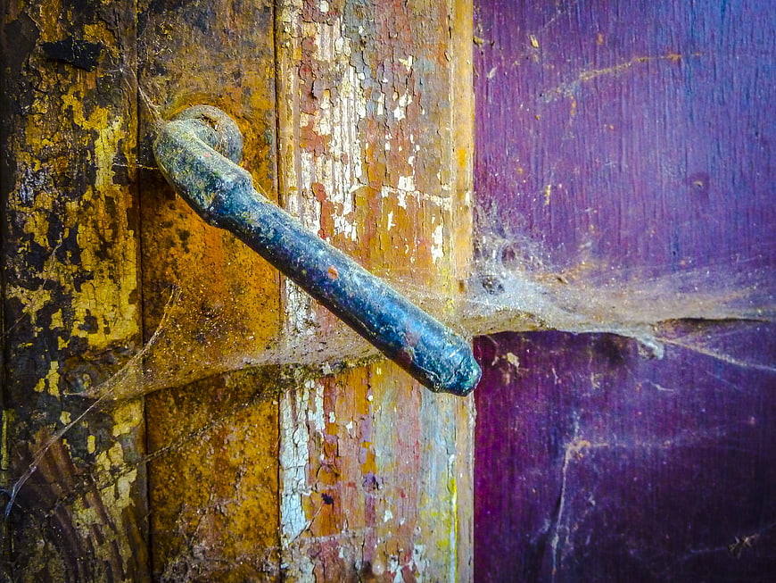 Close-up of rusty metal handle on weathered wooden door with cobwebs