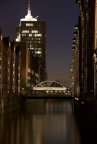 Night view of Speicherstadt canal with illuminated bridge and skyscraper