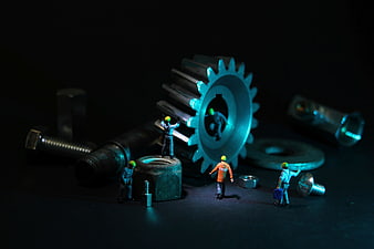 Miniature construction workers repairing giant metal gear and bolts