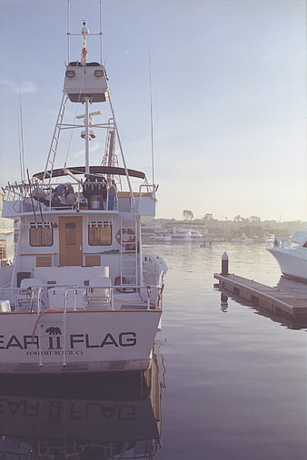 White fishing boat docked at marina with calm water reflection