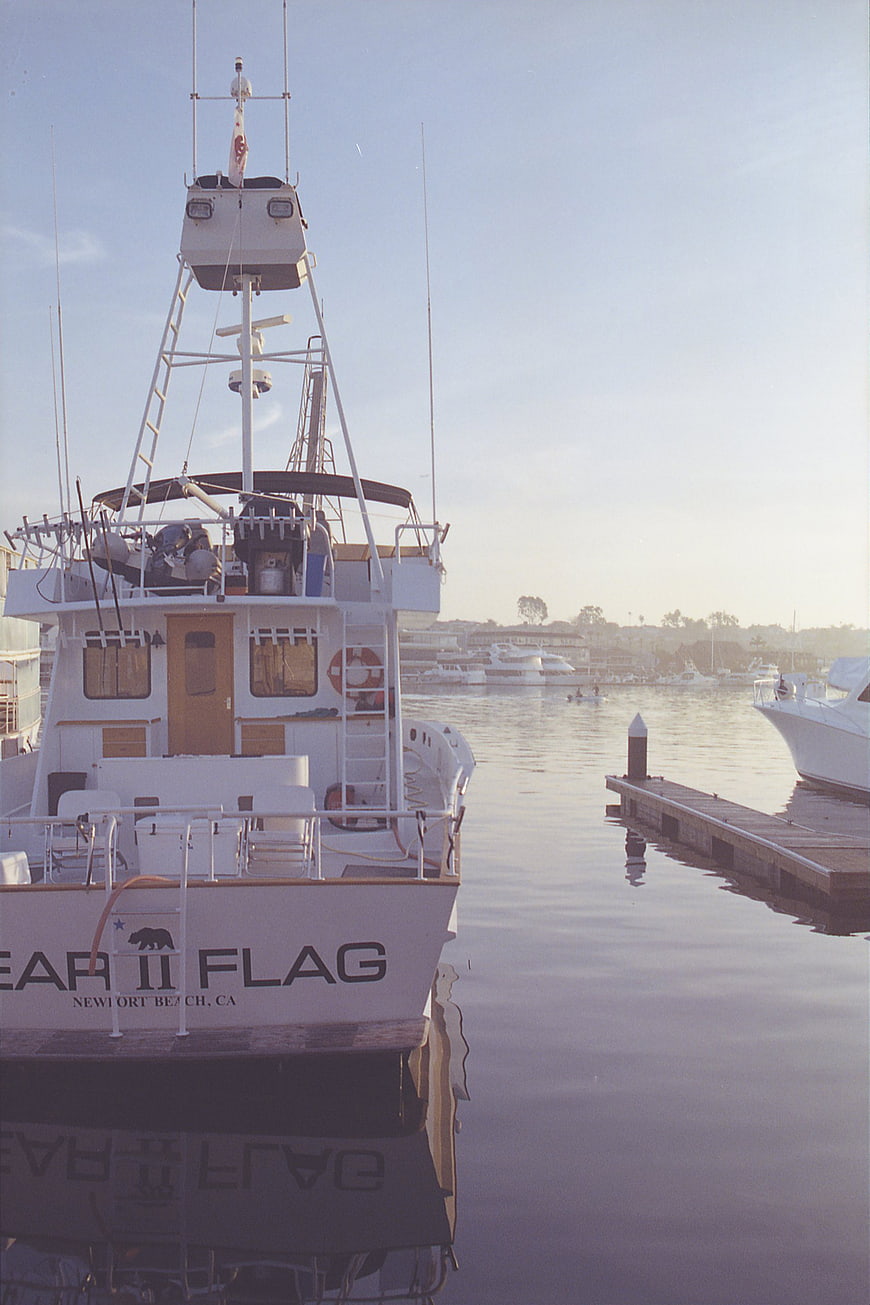 White fishing boat docked at marina with calm water reflection