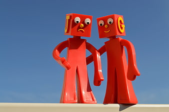 Two red toy figures with letters J and G on heads against blue sky