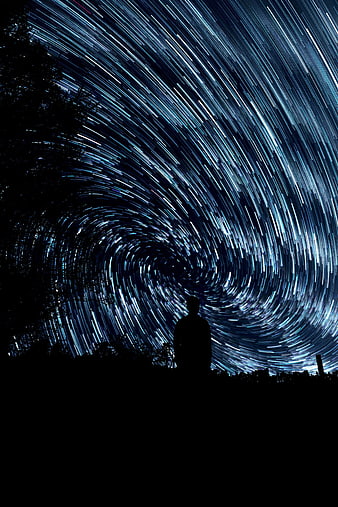 Silhouette of Man Under Swirling Star Trails Night Sky