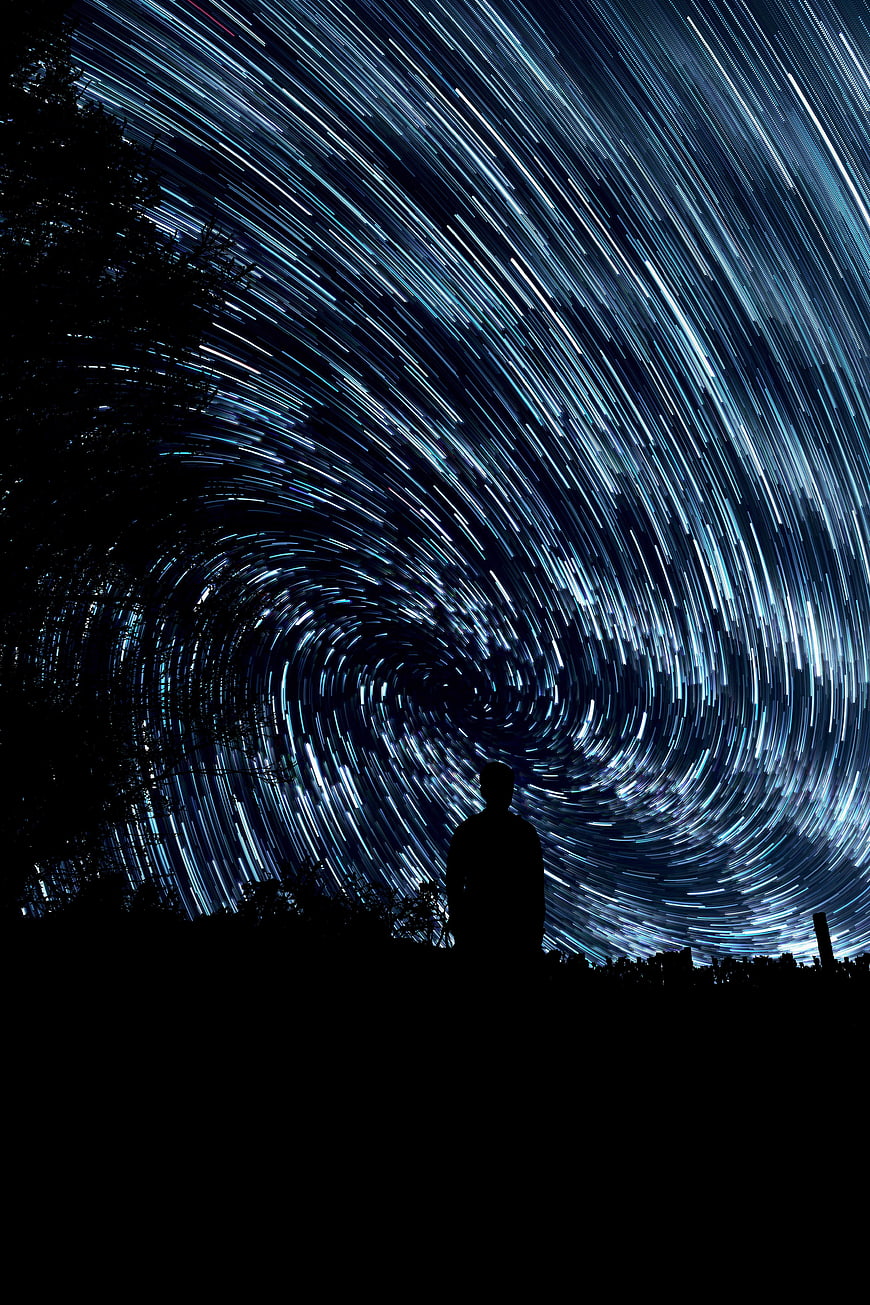 Silhouette of Man Under Swirling Star Trails Night Sky
