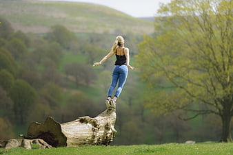 Woman balancing on tree stump in green nature landscape