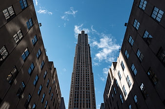 Low angle view of skyscraper between buildings against blue sky