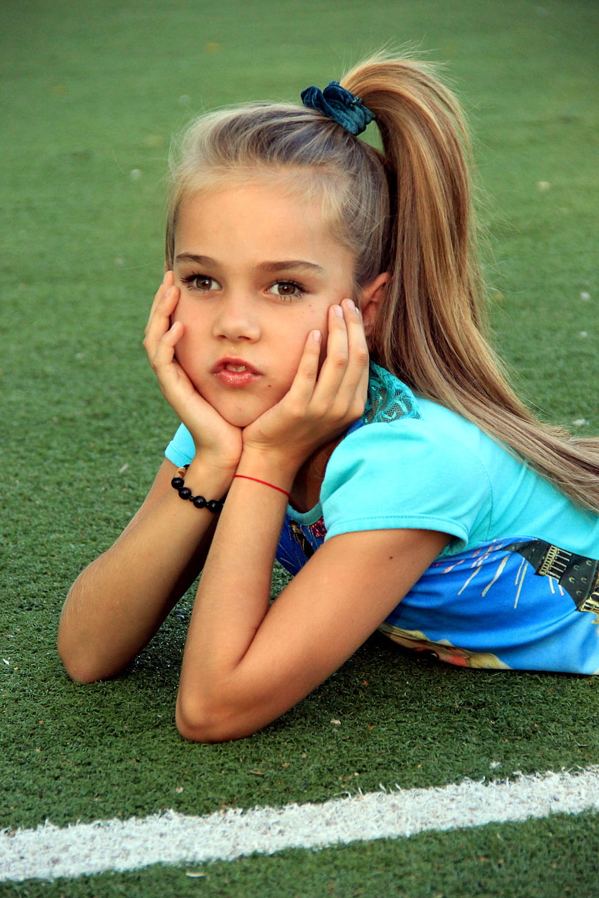 Portrait of young girl lying on green sports field
