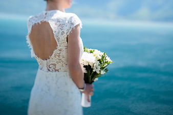 Bride in Lace Wedding Dress Holding Bouquet by Ocean