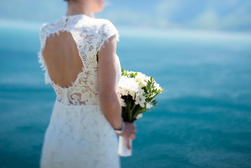 Bride in Lace Wedding Dress Holding Bouquet by Ocean
