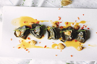 Gourmet stuffed grape leaves with shrimp and sauce on white plate