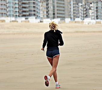 Woman jogging on sandy beach with city skyline background