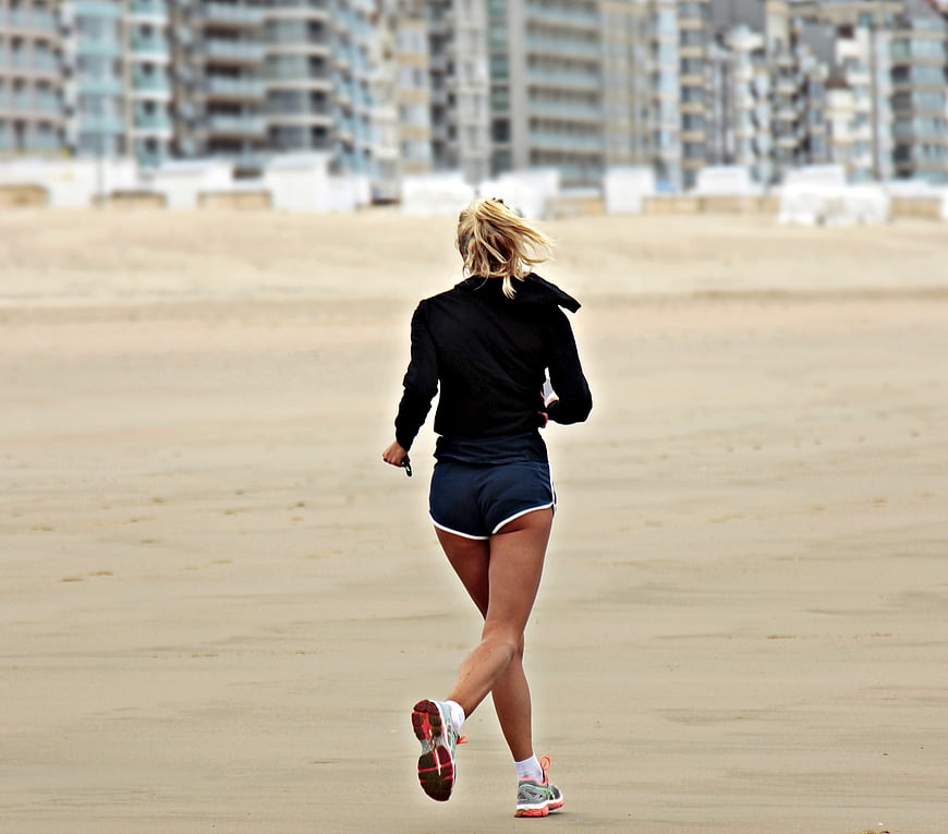 Woman jogging on sandy beach with city skyline background