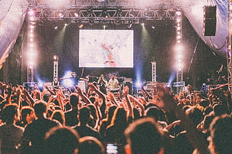 Live concert crowd with raised hands facing stage and band