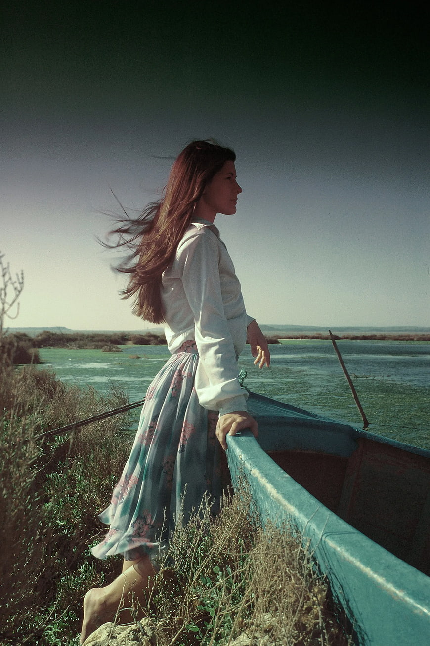Woman in Floral Dress Standing by Blue Boat in Marsh