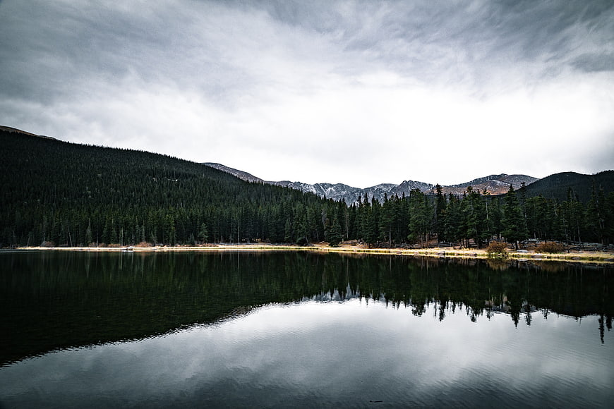 Serene Mountain Lake with Forest Reflection and Cloudy Sky