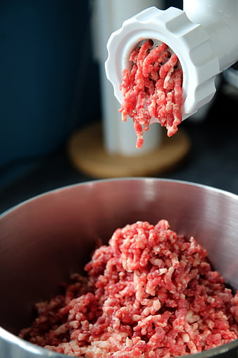 Fresh ground beef extruding from a white meat grinder into a metal bowl