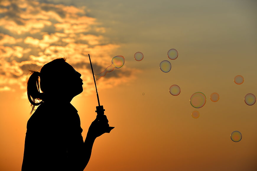 Silhouette of woman blowing soap bubbles at sunset