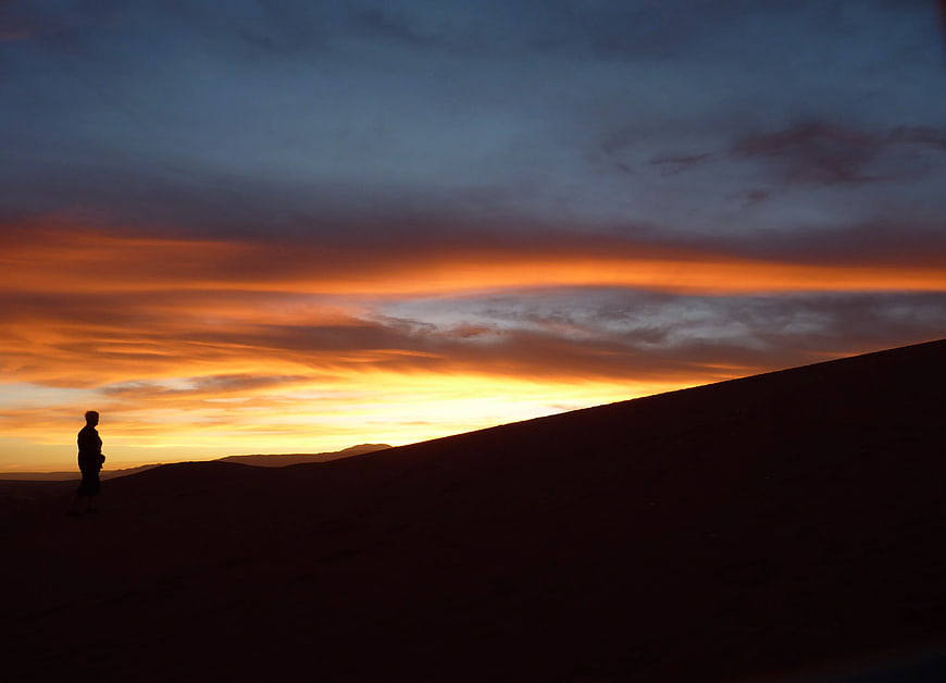 Silhouette of Person Standing on Sand Dune at Sunset