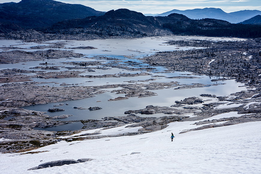 Hiker walking on snowy slope overlooking rocky alpine lake