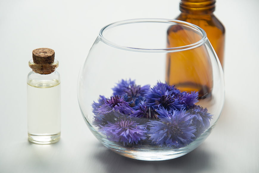Dried cornflowers in glass bowl with essential oil bottles