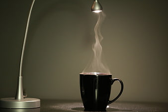 Steaming black coffee mug illuminated by a small desk lamp on a dark background