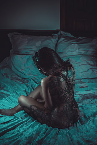 Tattooed Woman Sitting on Bed in Dark Moody Bedroom