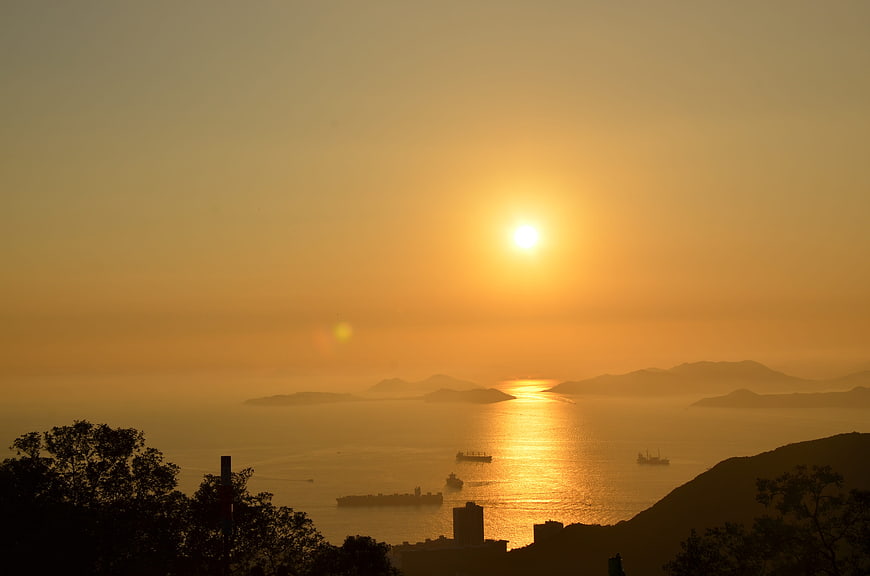 Golden Sunset Over Hong Kong Harbour With Silhouetted Ships And Mountains