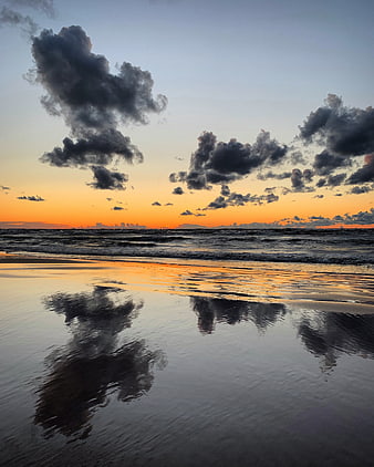 Dramatic sunset clouds reflecting on wet beach sand