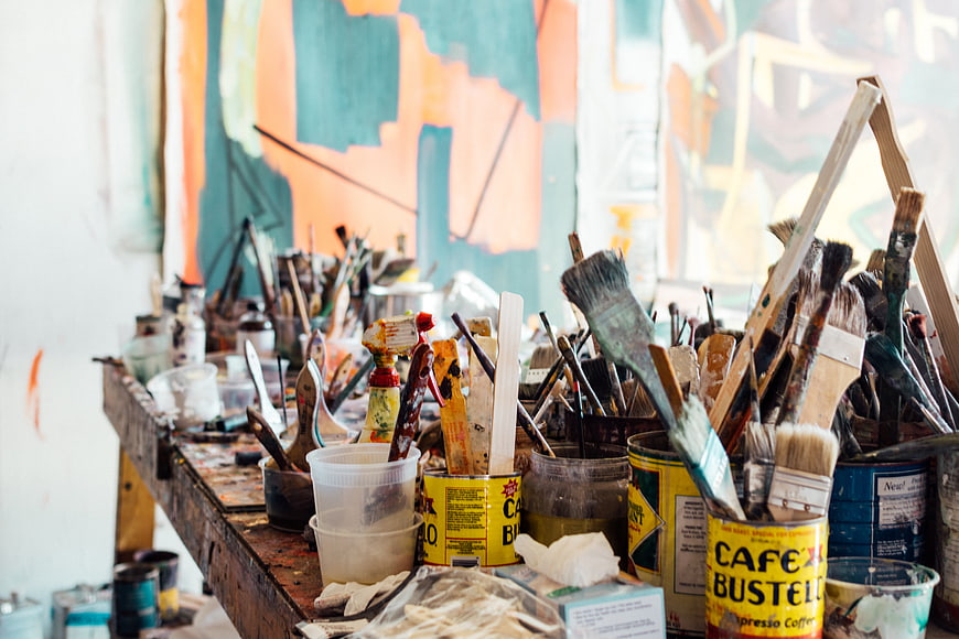 Cluttered artist workbench with paint brushes and supplies